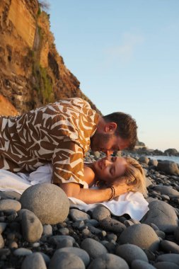 Karanlık çöktüğünde kayalık sahil şeridinde samimi bir an, güneş ışığıyla aydınlanan kıyı manzarası ve sakin dalgalar arasında spontane evlilik teklifi