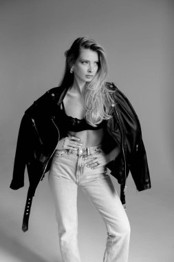 Moda mankeni kalın deri ceketli, kendine güvenen kot ve deri elbiseli bir kadının stüdyo fotoğrafı.