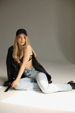 Model rahat, şık sarışın manken yerde yatıyor deri ceket ve yumuşak ışıklandırmalı kot pantolon giyiyor.