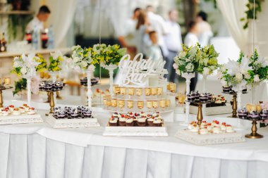 Çiçek ve ortam aydınlatması arasında çeşitli hamur işleri sergilenen sofistike resepsiyon tatlı aranjmanı