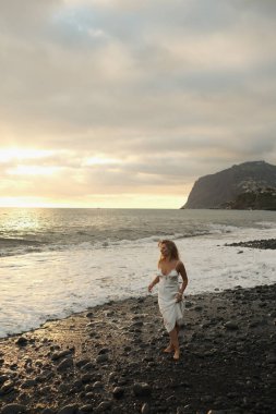 Kayalık sahilde huzurlu bir akşamın tadını çıkaran kadın figürü, Stony Beach 'te günbatımında rahatça geziniyor.