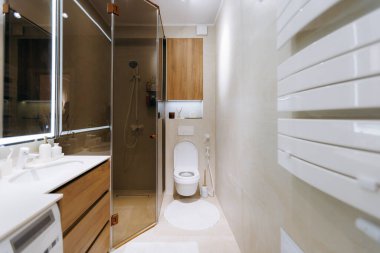 Entegre çamaşır makinesi, cam duş, duvar monteli tuvalet, ahşap kibir, verimli depolama çözümleri olan kompakt banyo.,