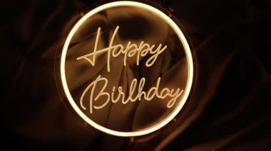 Neon mutlu doğum günü tabelası koyu kumaşa karşı parlayan altın, yüksek enerjili gece hayatı titreşimi ince spot ışıkları, çatı salonu