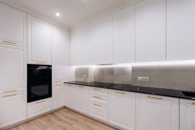 Çağdaş beyaz mutfak dolabı siyah fırın ve şık tezgah, temiz donanım ve kuvars yüzeyi olan aletler.