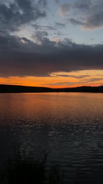Gün doğumu dalgalanan göl suyunda parlıyor, pastel gökyüzü altın ve maviyle çizilmiş, sisli su hattı, hafif bir esinti.