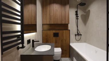 Ahşap dolabı, lavabosu ve küveti olan modern banyo, tasarımcı siyah armatürleri ve sıcak kabin altı aydınlatması