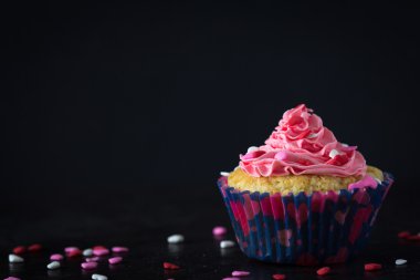 Cupcake tek ve buzlanma koyu arka plan üzerinde dağınık Sprinkles ile pembe
