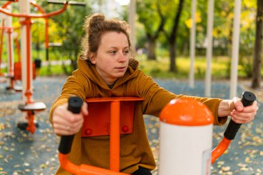 Genç bir kadın fiziksel egzersiz yapıyor, spor yapıyor, spor yapıyor, sokakta ve dışarıda eğitim ekipmanlarında spor yapıyor.