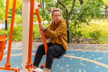 Genç bir kadın fiziksel egzersiz yapıyor, spor yapıyor, spor yapıyor, sokakta ve dışarıda eğitim ekipmanlarında spor yapıyor.