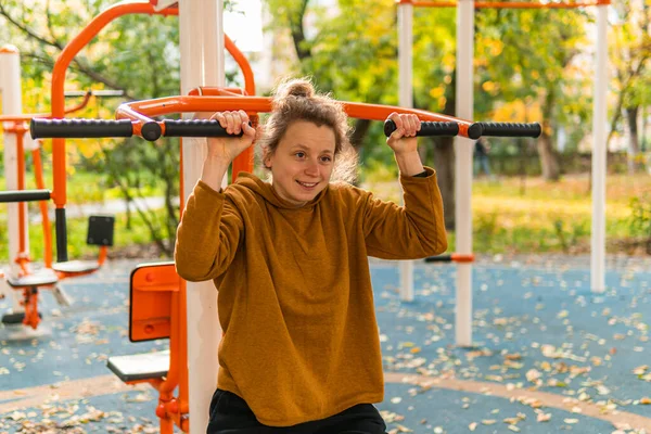 A young woman is doing physical exercises, sports, fitness on the training equipment on the street, outdoors