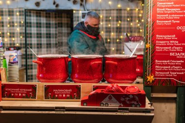 Kyiv (Kiev), Ukrayna - 19 Aralık 2020: Maskeli ve eldivenli bir satıcı Noel şenlikli içecekler pişiriyor ve satıyor, sıcak şarap içiyor