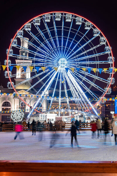 Киев (Киев), Украина - 6 января 2021 года: Многие люди и дети катаются на коньках возле большого колеса обозрения