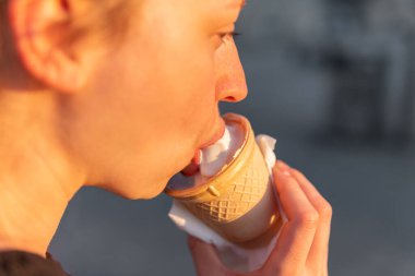 Genç bir kadın dondurma külahını tutuyor, yiyor ve eğleniyor.