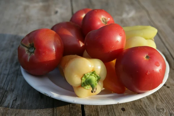 Red tomatoes and yellow sweet peppers on a white plate on a wooden table — Stock Photo, Image