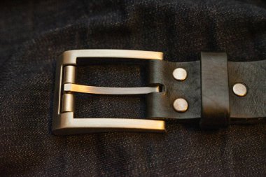 Koyu mavi kot pantolon üzerine basit dikdörtgen demir tokalı deri kemer.