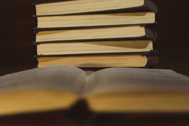 Bir yığın kitabın arka planında açık bir kitap. Kitap okuyordum. Kütüphane masasının üzerindeki eski bir kitabın seçici odak noktası ve yüzeysel alan derinliği