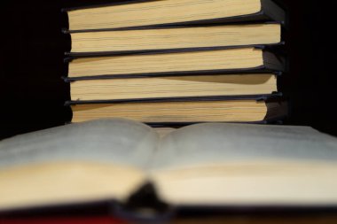 Bir yığın kitabın arka planında açık bir kitap. Kitap okuyordum. Kütüphane masasının üzerindeki eski bir kitabın seçici odak noktası ve yüzeysel alan derinliği