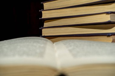 Bir yığın kitabın arka planında açık bir kitap. Kitap okuyordum. Kütüphane masasının üzerindeki eski bir kitabın seçici odak noktası ve yüzeysel alan derinliği