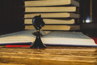 Açık bir kitabın arka planında satranç taşı Kara Şövalye.