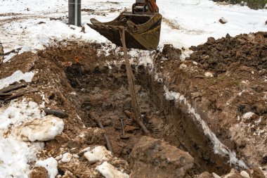 Kışın ısıtma ve elektrik iletişiminin tamiri. Kazı kovası kazıyor..