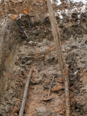 Yeraltı hizmetleri için kil toprağında bir çukur kazılmış. Boru döşemek için toprağı kazmaya çalış..