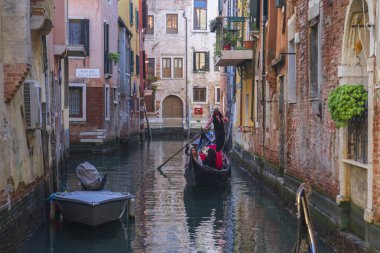 Venedik, İtalya - 10.11.2024: gandolcu Venedik 'teki dar kanal boyunca geleneksel gondolda turist yolcu taşıyor.