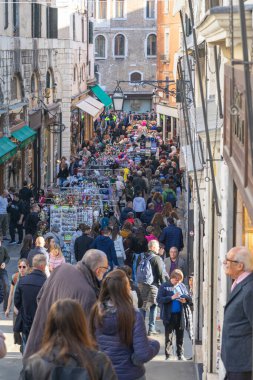Venedik, İtalya - 10.11.2024: Venedik 'in tarihi sokaklarında hareketli sokak pazarı. Kalabalık, parlak tentelerin altında hediyelik eşya, giysi ve aksesuar satan renkli satıcılara göz atıyor..