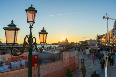 Venedik, İtalya - 10.11.2024: Venedik rıhtım güvertesi gün batımında sokak lambası ve bazilika manzaralı.