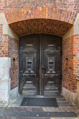 Collegium Maius, Krakow, Polonya 'nın kırmızı tuğlalı girişinde dekoratif oymalarla süslenmiş koyu renk ahşap bir kapı.