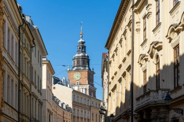 Krakow Belediye Binası Kulesi 'nin mavi gökyüzünün altında tarihi binaların üzerinde yükselen bir saatle görüntüsü, Polonya