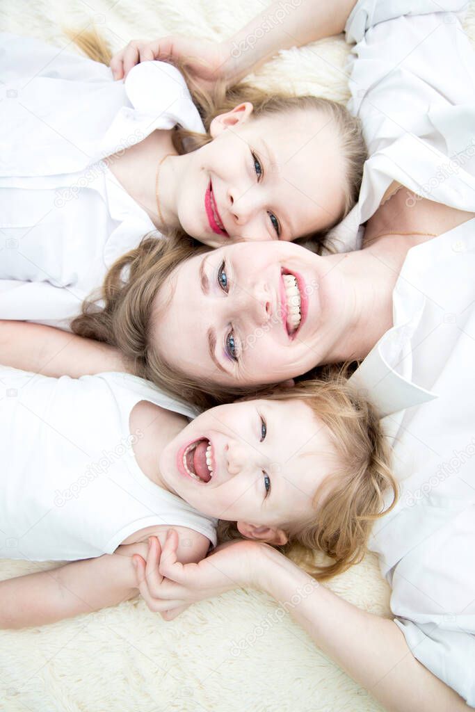 Portrait of mom and her daughters smiling on the bed topview.