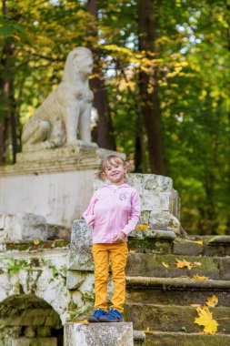 Kolu kırık bir kız eski bir parkın merdivenlerinde duruyor.