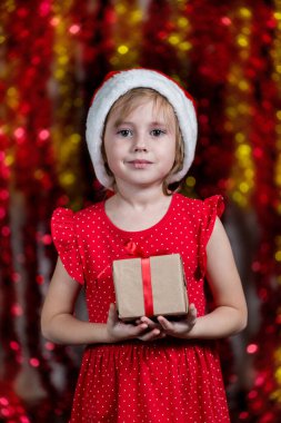 Noel Baba Şapkalı Şirin Kız Noel hediyesini tutuyor ve kameraya gülümsüyor..