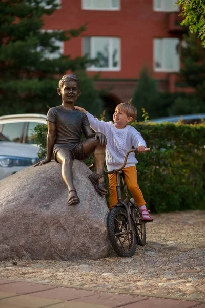 Kısa Saçlı Küçük Bir Kızın Portresi Bir Bisikletçinin Anıtına Oturmuş — Stok fotoğraf