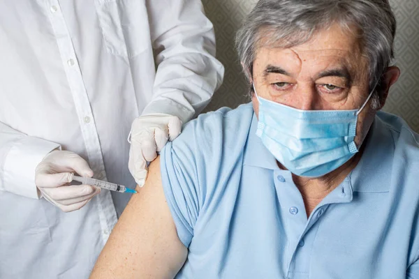 Yaşlı bir adam bir erkek doktor tarafından koronavirüse karşı aşı oluyor. Yaşlı bir hastayı grip, grip, zatürree veya koronavirüse karşı aşılayan pratisyen hekimler.