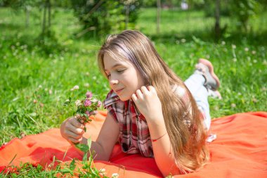 15 yaşında Kafkas görünümlü genç bir kız güneş ve havanın tadını çıkarıyor ve bir yaz günü parkta çimlerin üzerinde bir buket yabani çiçek yatıyor. Kız ekose gömlek giymiş. 