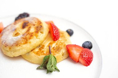 Breakfast with mini cheesecakes, fresh blueberries and strawberry slices on white plate
