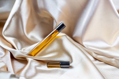 İpek kumaşın kıvrımlarında duran koyu camdan yapılmış kozmetik ürünleri depolamak için bir kap. Kokulu kozmetik güzellik ürünü..