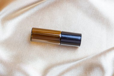 İpek kumaşın kıvrımlarında duran koyu camdan yapılmış kozmetik ürünleri depolamak için bir kap. Parfüm, serum ya da losyon şişesi.