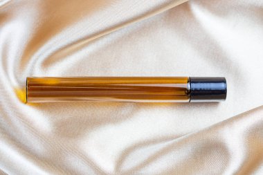 İpek kumaşın kıvrımlarında duran koyu camdan yapılmış kozmetik ürünleri depolamak için bir kap. Parfüm, serum ya da losyon şişesi.