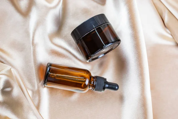 İpek kumaşın kıvrımlarında duran koyu camdan yapılmış kozmetik ürünleri depolamak için bir kap. Kokulu kozmetik güzellik ürünü..