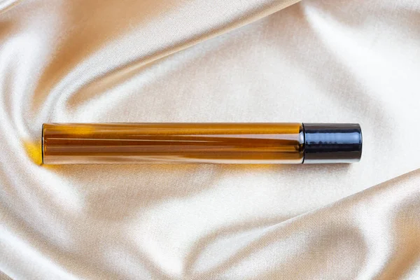 İpek kumaşın kıvrımlarında duran koyu camdan yapılmış kozmetik ürünleri depolamak için bir kap. Parfüm, serum ya da losyon şişesi.