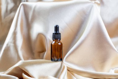 İpek kumaşın kıvrımlarında duran koyu camdan yapılmış kozmetik ürünleri depolamak için bir kap. Kokulu kozmetik güzellik ürünü..