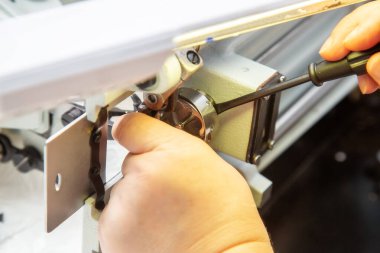 Tornavidayla kadın elleri dikiş makinesinin mekiğini tamir ediyor. Evdeki endüstriyel dikiş makinesinin tamiri. Bakım.