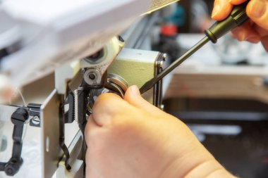 Tornavidayla kadın elleri dikiş makinesinin mekiğini tamir ediyor. Evdeki endüstriyel dikiş makinesinin tamiri. Bakım.