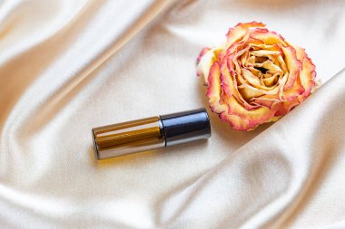 Kurumuş gül çiçekleriyle çevrili ipek kumaş kıvrımlarında koyu camdan yapılmış kozmetik ürünleri depolamak için konteyner. Kokulu kozmetik güzellik ürünü..