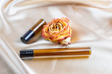 Kurumuş gül çiçekleriyle çevrili ipek kumaş kıvrımlarında koyu camdan yapılmış kozmetik ürünler depolamak için çeşitli kaplar bulunur. Parfüm, serum ya da losyon şişesi.