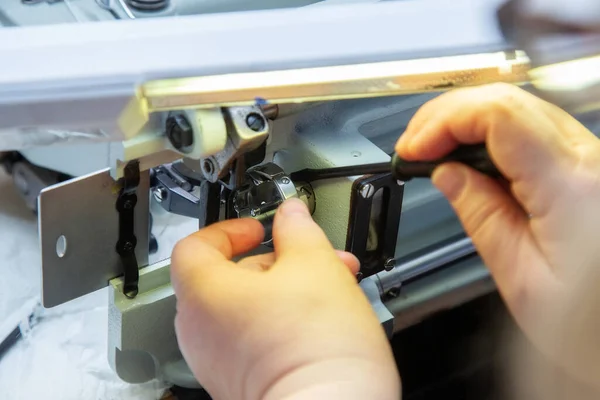 Female hands with a screwdriver repair the shuttle of the sewing machine. Repair of an industrial sewing machine at home. Maintenance.