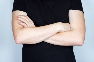 Siyah tişörtlü bir adam ellerini çapraz yapıp kameraya bakıyor. Gri arkaplanda izole edilmiş, başsız kesilmiş fotoğraf..