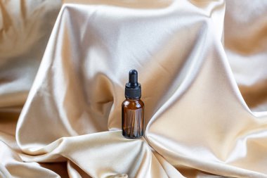 İpek kumaşın kıvrımlarında duran koyu camdan yapılmış kozmetik ürünleri depolamak için bir kap. Parfüm, serum ya da losyon şişesi.